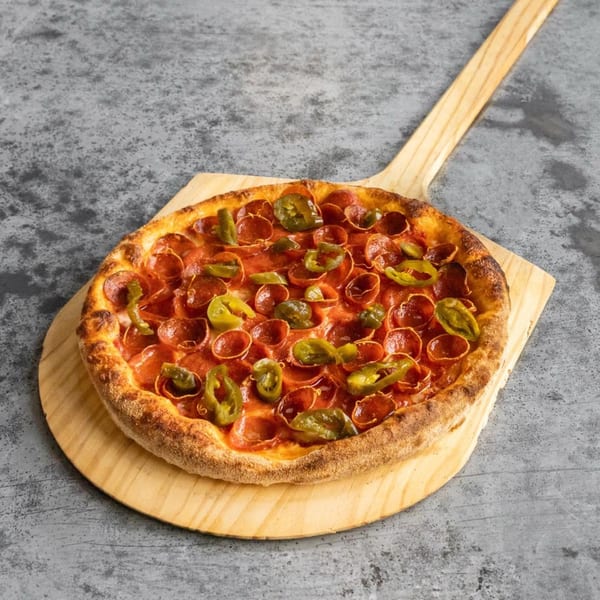 TuscNY Pizza's pepperoni and jalapeño pizza on a wooden pizza peel against a gray background.