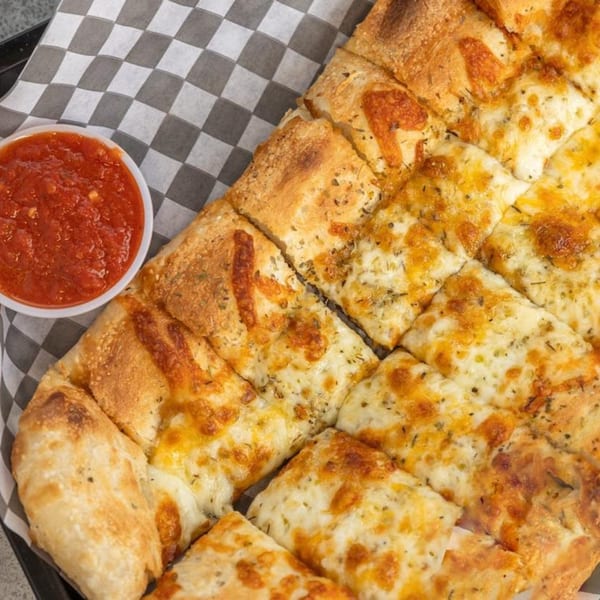 TuscNY Pizza's cheesy garlic breadsticks with herbs, served with a side of marinara sauce.