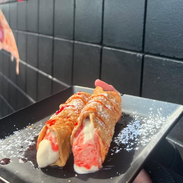 Two cannolis with white and red filling, powdered sugar, and syrup on a black plate.