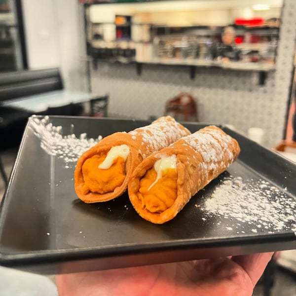Two pumpkin cannolis with white cream filling and powdered sugar on a black tray.