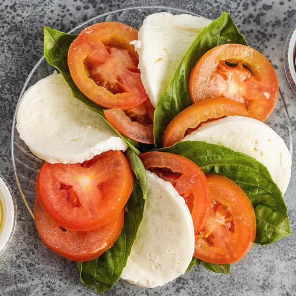 Caprese salad with sliced tomatoes, fresh mozzarella, and basil leaves on a clear plate.